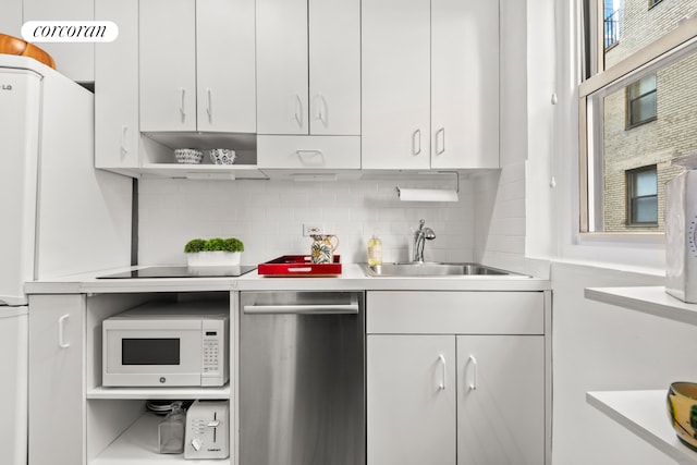 kitchen with white microwave, white cabinetry, light countertops, and a sink