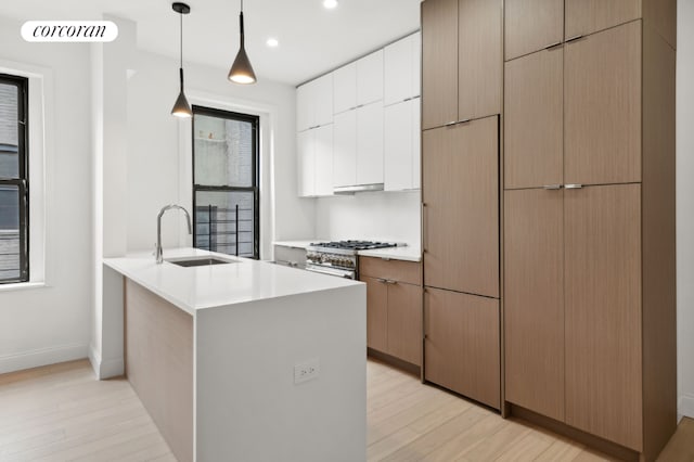 kitchen with light wood-type flooring, kitchen peninsula, white cabinetry, hanging light fixtures, and sink