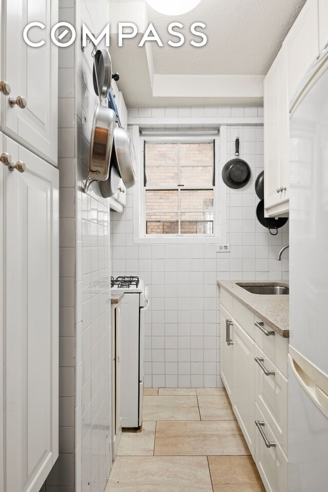 kitchen featuring light stone counters, a sink, white cabinets, gas range, and white refrigerator