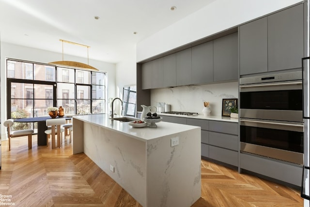 kitchen with sink, gray cabinetry, a kitchen island with sink, stainless steel appliances, and light parquet flooring