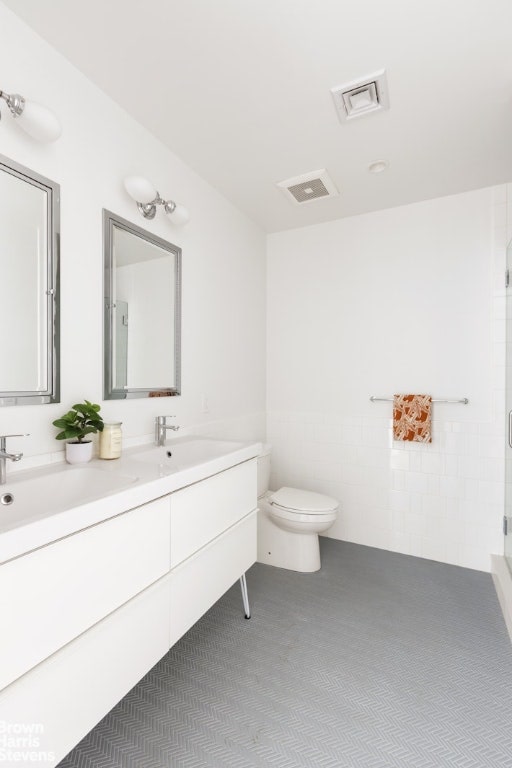 bathroom with walk in shower, vanity, toilet, and tile walls