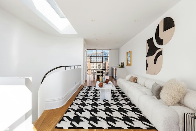 living room featuring a wall of windows, wood-type flooring, and a skylight