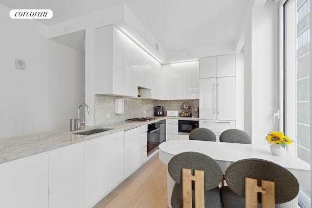 kitchen featuring sink, white cabinets, decorative backsplash, light stone counters, and black appliances