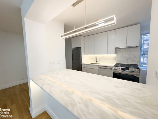 kitchen featuring dishwashing machine, stainless steel gas range oven, black refrigerator, a sink, and modern cabinets