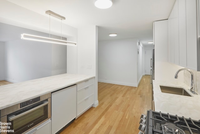 kitchen with a sink, stainless steel appliances, light wood-style flooring, white cabinetry, and baseboards