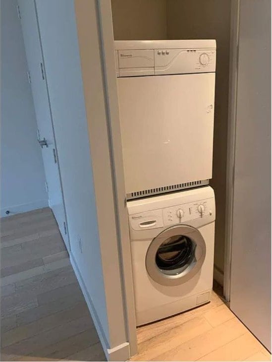 laundry room featuring stacked washer / drying machine and light wood-type flooring