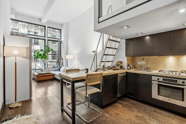 kitchen with stainless steel appliances, dark wood-style flooring, a sink, light countertops, and beamed ceiling