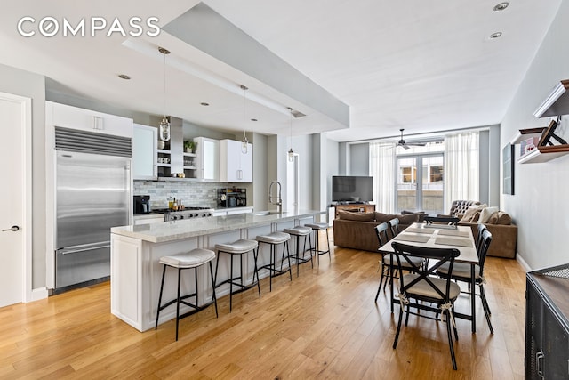 kitchen with a breakfast bar, light wood finished floors, open shelves, backsplash, and stainless steel built in refrigerator