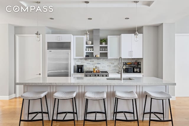 kitchen with a sink, light wood finished floors, stainless steel built in fridge, tasteful backsplash, and a kitchen bar