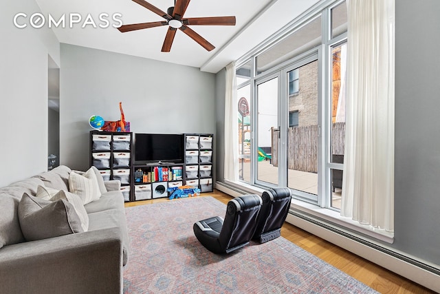 living area featuring a baseboard heating unit, ceiling fan, wood finished floors, and a wealth of natural light