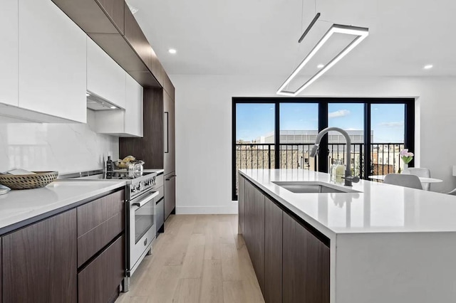 kitchen with a center island with sink, high end range, light countertops, white cabinetry, and a sink