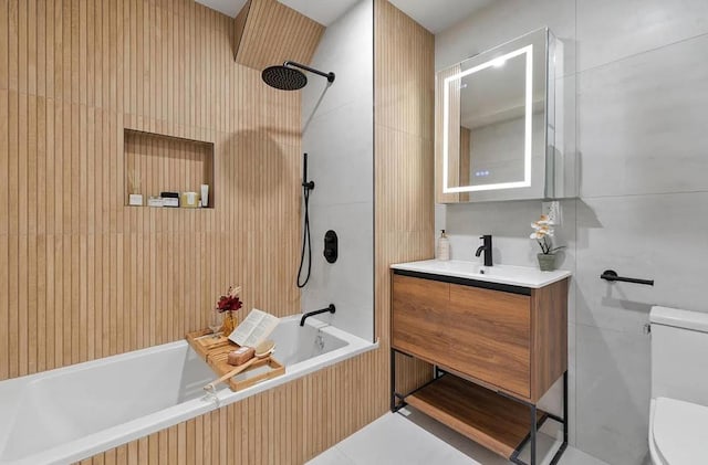 full bathroom with tile walls, tiled shower / bath, toilet, and vanity