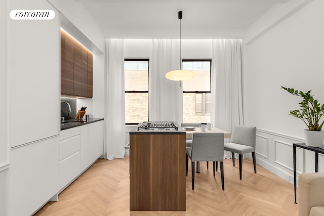 kitchen with white cabinets, dark countertops, a sink, modern cabinets, and wainscoting