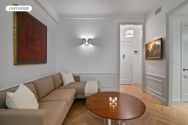 living room featuring wainscoting, visible vents, ornamental molding, and a decorative wall