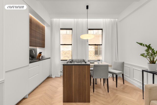 kitchen featuring a wainscoted wall, modern cabinets, dark countertops, white cabinetry, and a decorative wall