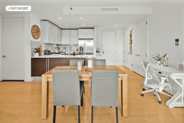 kitchen featuring visible vents, light wood finished floors, stainless steel fridge with ice dispenser, and white cabinetry