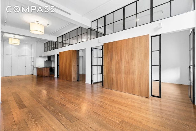 unfurnished living room with beam ceiling, light hardwood / wood-style floors, and a high ceiling