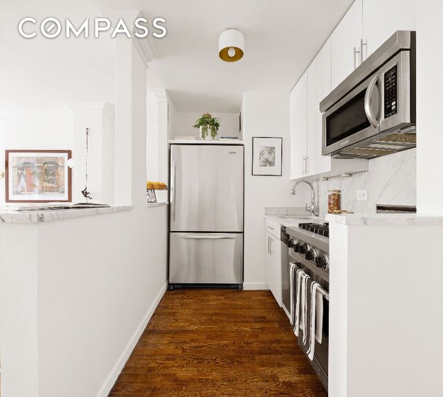 kitchen with appliances with stainless steel finishes, tasteful backsplash, sink, white cabinets, and dark wood-type flooring