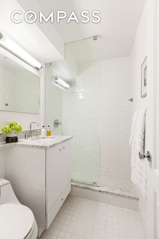 bathroom featuring vanity, a tile shower, and toilet