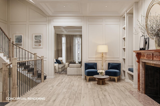 sitting room with coffered ceiling, wood finished floors, crown molding, a decorative wall, and a high end fireplace