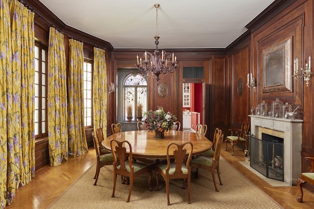 dining room with wood walls, ornamental molding, a premium fireplace, and a notable chandelier