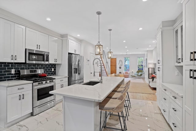 kitchen with marble finish floor, stainless steel appliances, open floor plan, white cabinetry, and a sink