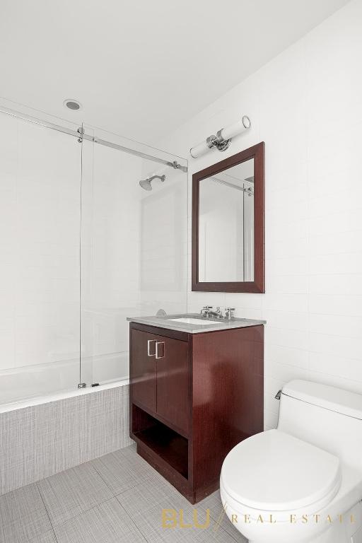 bathroom with toilet, tile patterned floors, tiled shower / bath, vanity, and tile walls