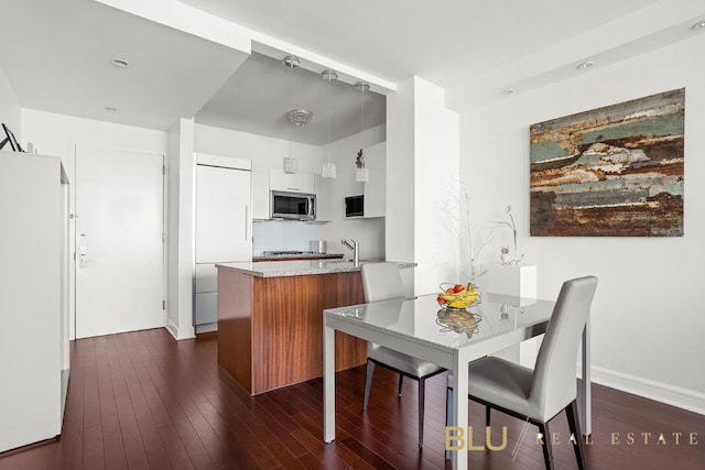 kitchen featuring dark wood-style floors, stainless steel microwave, freestanding refrigerator, paneled built in refrigerator, and a peninsula