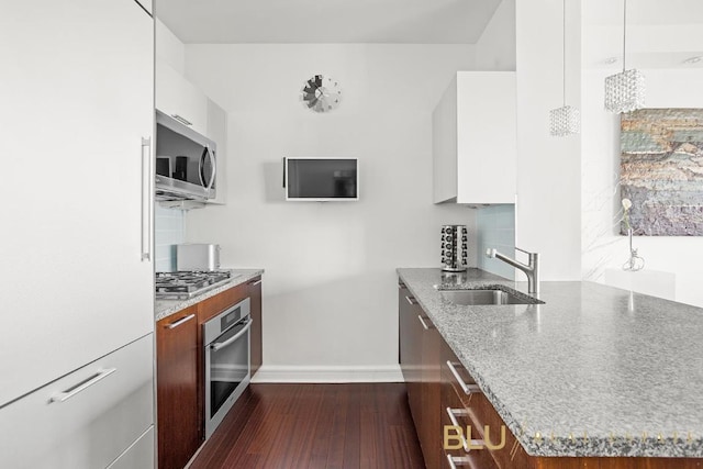 kitchen with decorative light fixtures, stainless steel appliances, white cabinetry, a sink, and light stone countertops