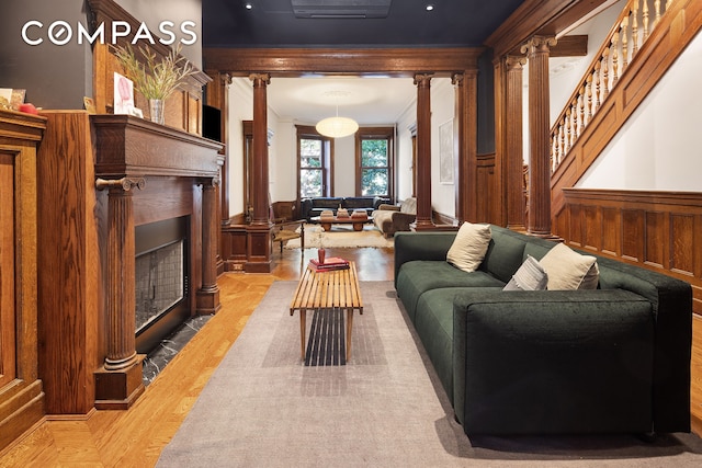 living area featuring decorative columns, a wainscoted wall, a fireplace with flush hearth, stairs, and crown molding