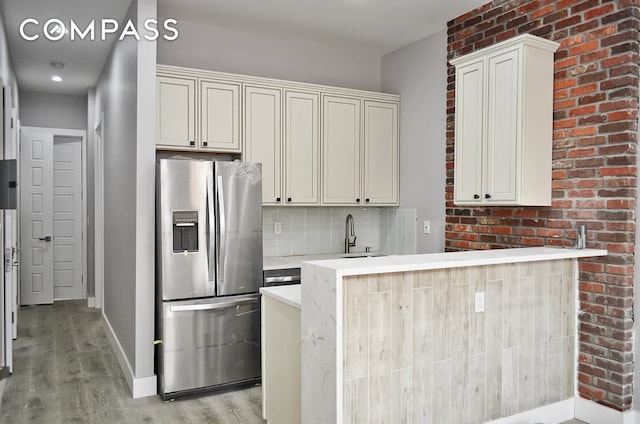 kitchen with light wood finished floors, a sink, tasteful backsplash, stainless steel fridge with ice dispenser, and light countertops