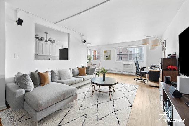 living area with a baseboard heating unit, a wall unit AC, and light wood-style flooring