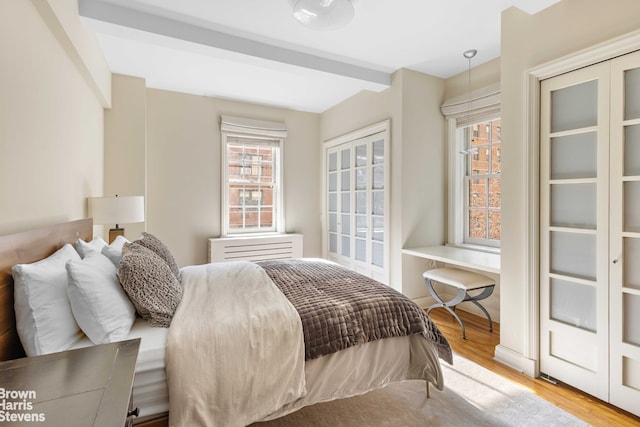 bedroom with beamed ceiling, multiple windows, and light wood-type flooring