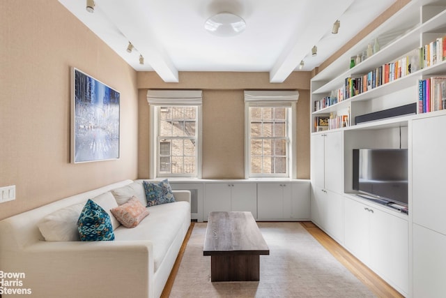 living room featuring beamed ceiling, rail lighting, and light hardwood / wood-style floors