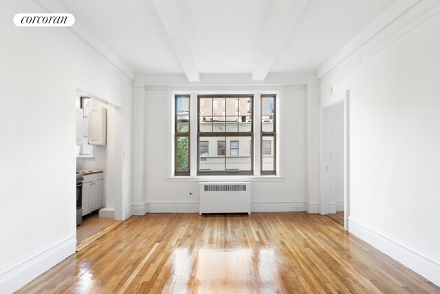 spare room featuring light hardwood / wood-style floors, beamed ceiling, and radiator