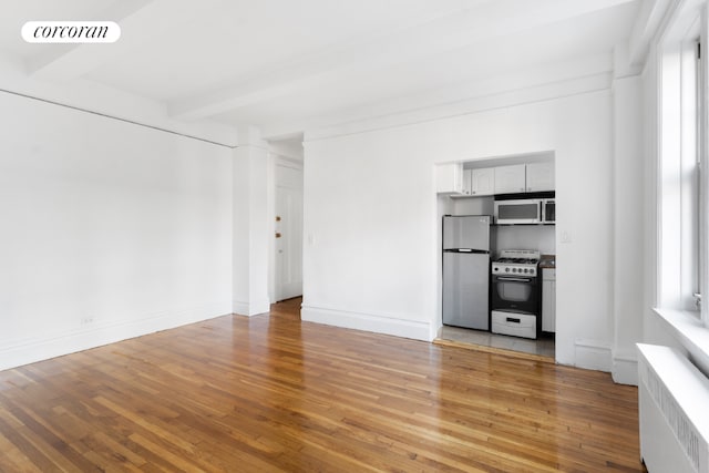 unfurnished living room featuring beam ceiling, radiator heating unit, plenty of natural light, and light wood-type flooring