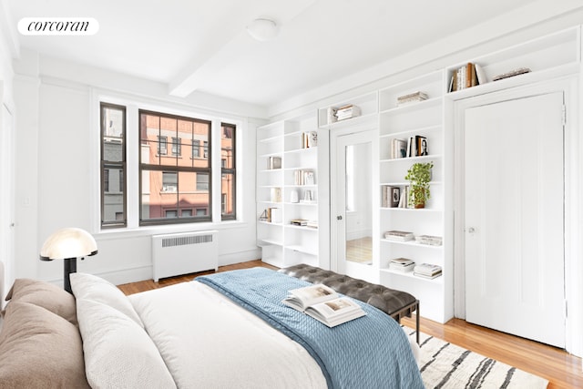 bedroom with light wood-type flooring, radiator heating unit, and beam ceiling