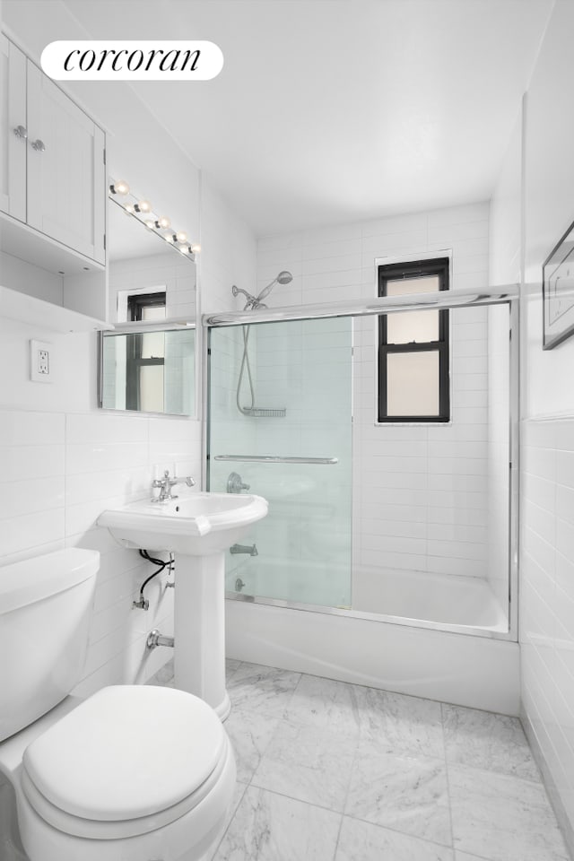 bathroom with toilet, tile walls, combined bath / shower with glass door, and marble finish floor