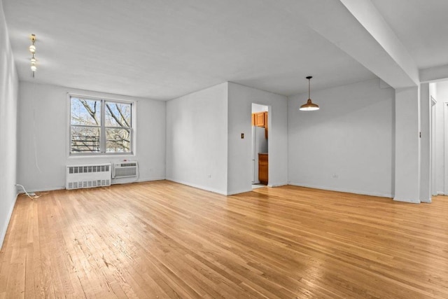 unfurnished living room featuring radiator heating unit, light hardwood / wood-style flooring, and an AC wall unit