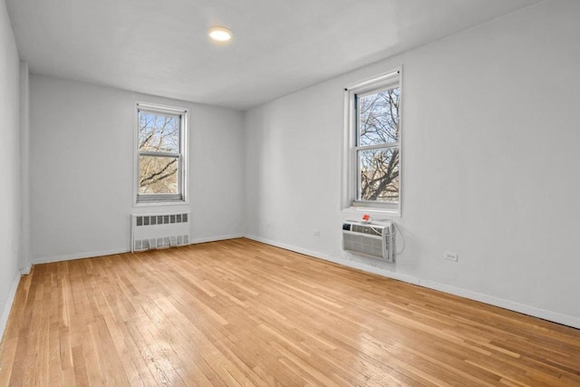 spare room featuring a wall mounted air conditioner, radiator, and light hardwood / wood-style floors