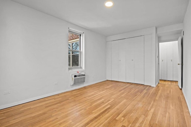 unfurnished bedroom with a closet, a wall mounted AC, and light hardwood / wood-style flooring