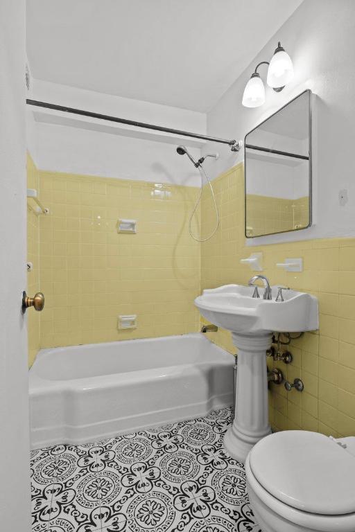 bathroom featuring tiled shower / bath, toilet, tile patterned flooring, and tile walls