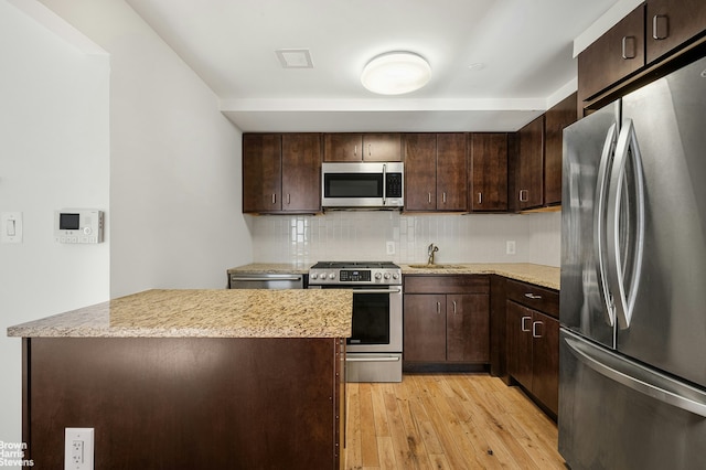 kitchen with appliances with stainless steel finishes, light wood-style floors, a sink, and dark brown cabinets