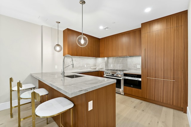 kitchen featuring stainless steel stove, a peninsula, a sink, brown cabinets, and decorative backsplash