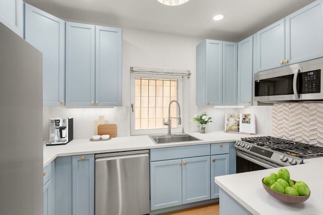 kitchen with appliances with stainless steel finishes, sink, blue cabinetry, and decorative backsplash