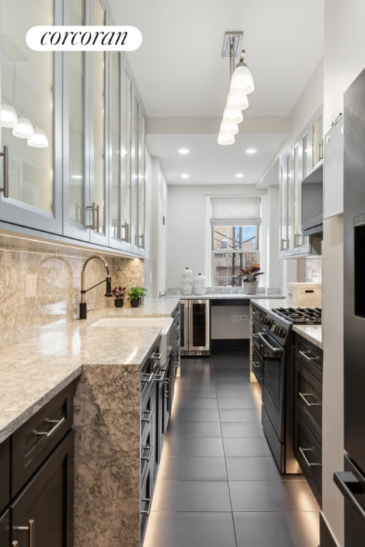 kitchen featuring hanging light fixtures, tasteful backsplash, light stone countertops, black range with gas stovetop, and beverage cooler