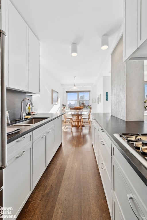 kitchen featuring dark wood-style floors, dark countertops, white gas cooktop, white cabinets, and a sink