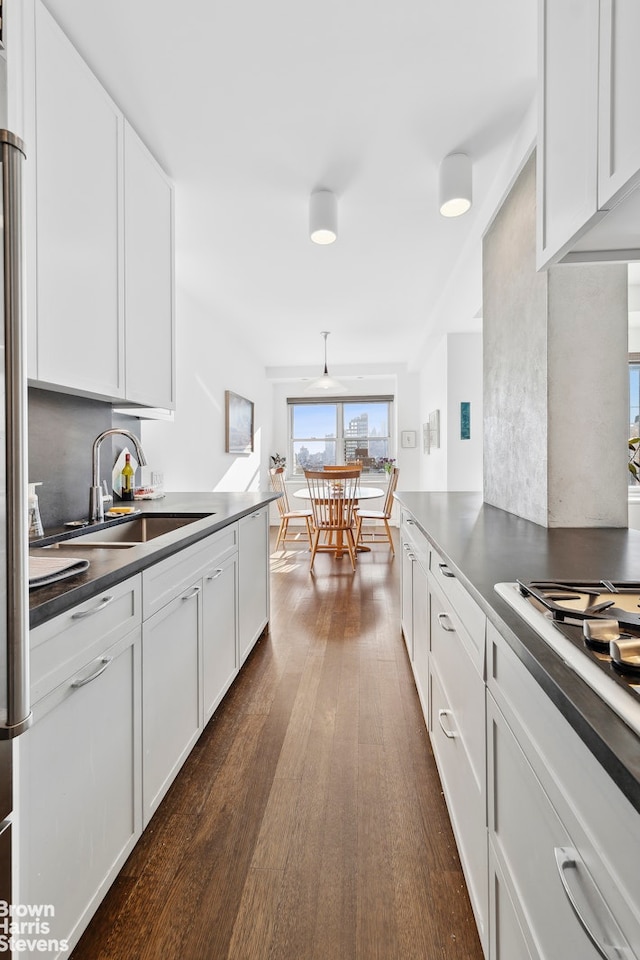 kitchen with dark wood-style flooring, dark countertops, white cabinetry, a sink, and gas cooktop