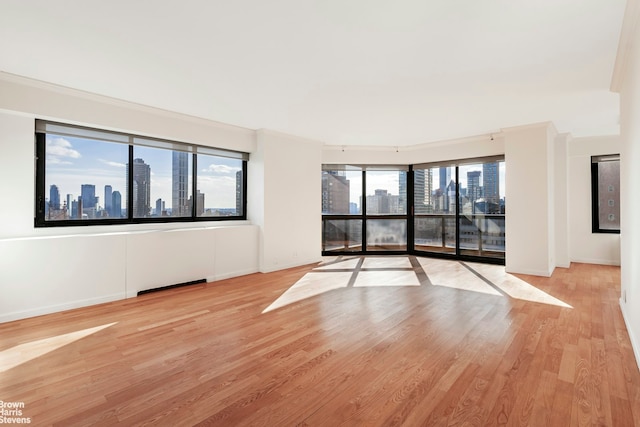 unfurnished room with light wood-style floors, a view of city, and baseboards