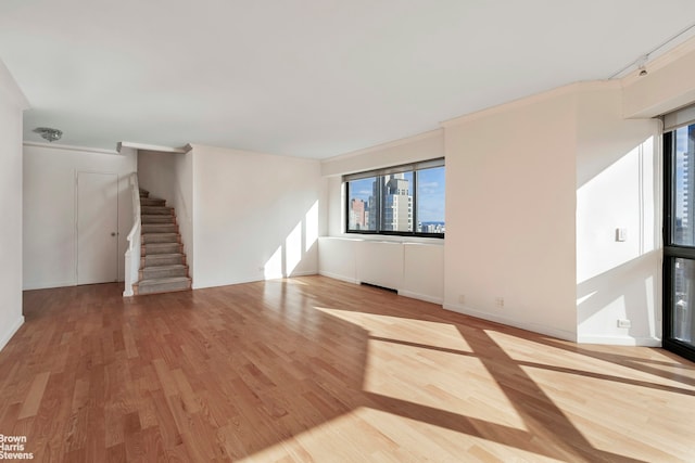 unfurnished living room featuring baseboards, stairs, ornamental molding, and wood finished floors